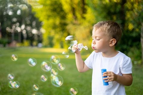 Premium Photo Cute Blonde Baby Inflates Soap Bubbles In Summer On A