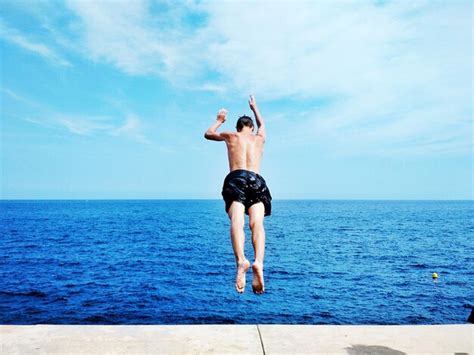 Premium Photo Rear View Of Shirtless Man Jumping Into Sea Against Sky