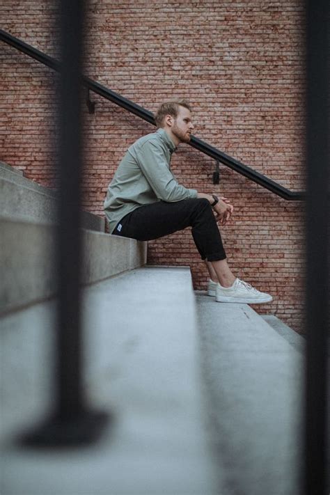 A Man Sitting On The Edge Of A Set Of Stairs With His Hand In His Pocket