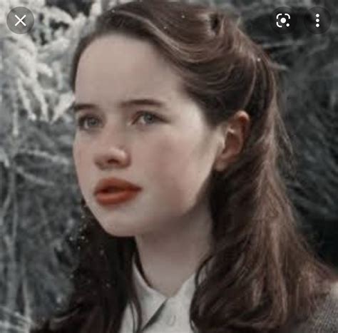 A Woman With Long Brown Hair Wearing A Suit And Orange Lipstick In