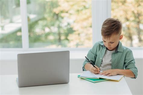 Adorable niño atento escribiendo en un cuaderno y usando una