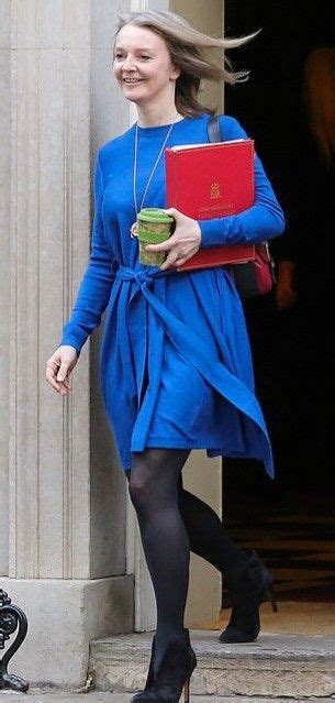 A Woman In A Blue Dress Holding A Red Laptop And Smiling While Walking