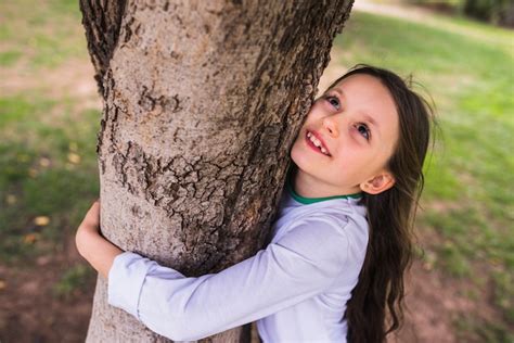 Souriante Petite Fille Embrassant Un Arbre Dans Le Jardin Photo Gratuite