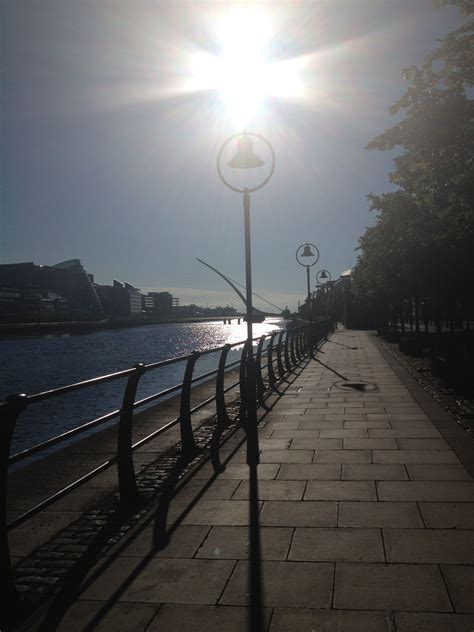 The Sun Shines Brightly On A Sidewalk Along The Waters Edge As It