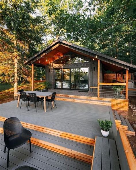 A Wooden Deck With Chairs And Tables In The Woods Next To A Small Cabin