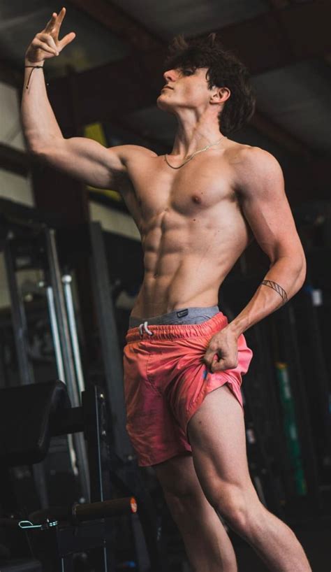 A Shirtless Man Standing In Front Of A Gym Machine With His Arm Raised Up