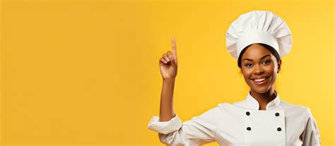 Black Female Chef Smiling And Pointing Upwards Wearing Uniform