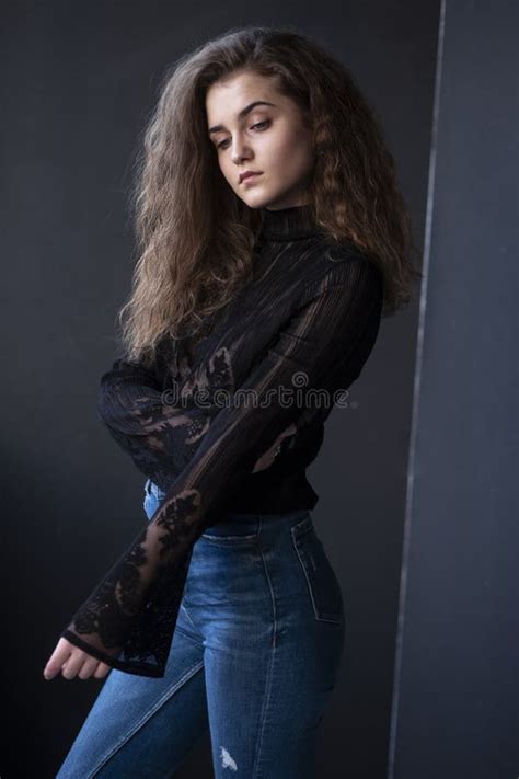 Beauty Image Of A Pretty Young Woman With Curly Hair Dressed In A Black Suitcase And Jeans