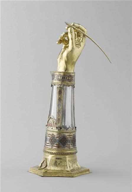 A Gold And Silver Vase With A Hand Holding A Flower In Its Mouth