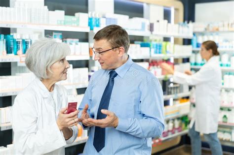 Male Customer Consulting With Mature Female Pharmacist At Pharmacy