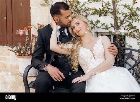 Portrait de jeune mariée blonde en robe blanche et marié brunet en costume embrassant et assis