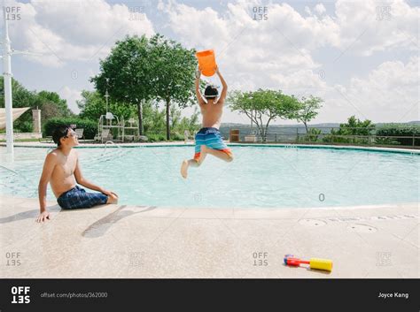 Boy jumping into a swimming pool while another teen looks on stock photo - OFFSET