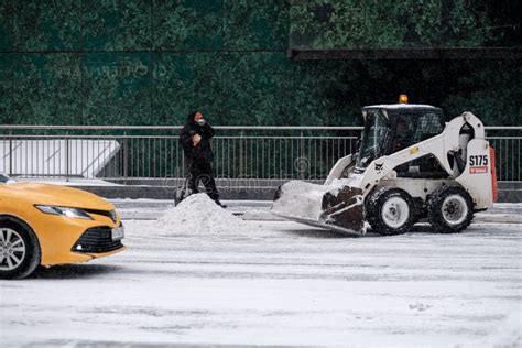 A Utility Worker And A Small Loader Excavator Remove Snow From The Road