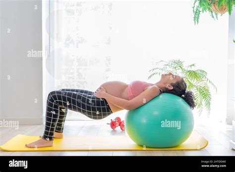 A Young Pregnant Woman Leaning On A Fitness Ball Does Exercises To