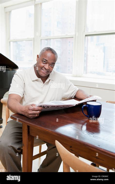 A Mature Man Sitting At Dining Table Holding A Newspaper Stock Photo