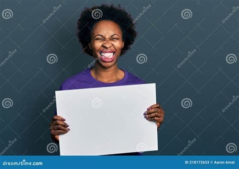 African American Woman With Afro Hair Holding Blank Empty Banner Sticking Tongue Out Happy With