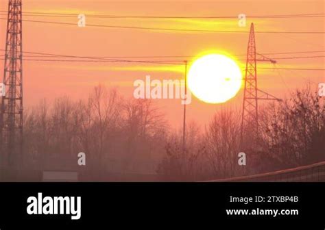 Enormous Sun On Peachy Orange Color Sky Setting Behind High Voltage