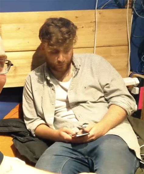 Two Men Sitting Next To Each Other In Front Of A Wooden Headboard And Wall