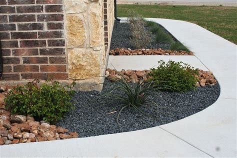 A Small Garden With Rocks And Plants In Front Of A Brick Building