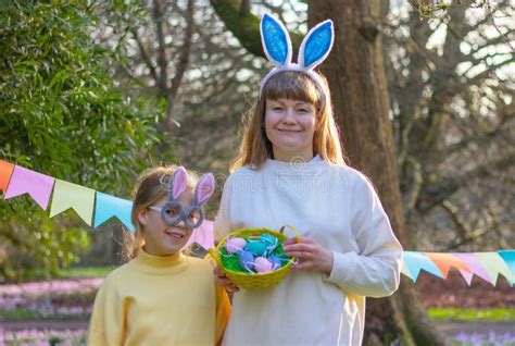 Woman And Girl With Rabbit Ears And Basket Of Colored Eggs In Park