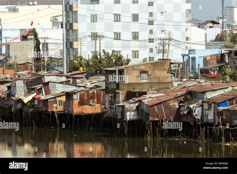 Slum Wooden House On The Saigon River Bank In Front Of Modern