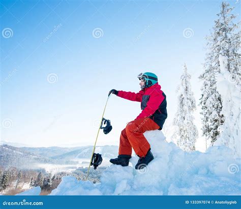 Man Snowboarder Sitting On Top Of A Snowy Hill With His Snowboard