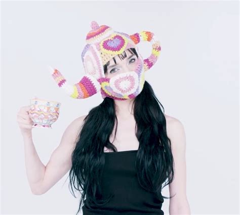 A Woman With Long Black Hair Wearing A Knitted Hat And Holding A Cup In