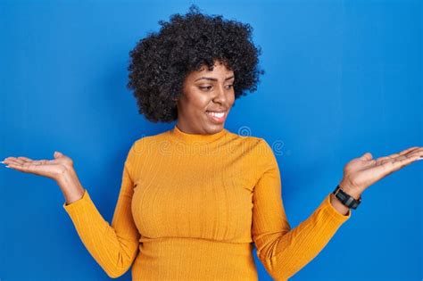 Black Woman With Curly Hair Standing Over Blue Background Smiling Showing Both Hands Open Palms