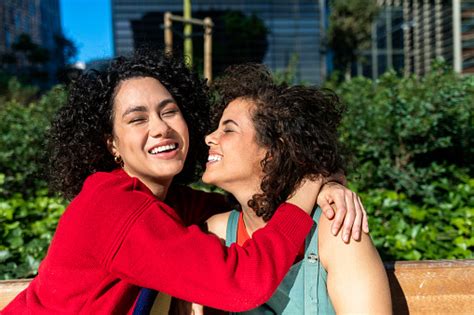 Smiling Lesbian Couple Embracing And Relaxing On A Park Bench Stock