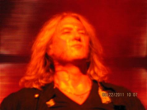 A Man With Long Blonde Hair Standing In Front Of A Red Light And Looking Up