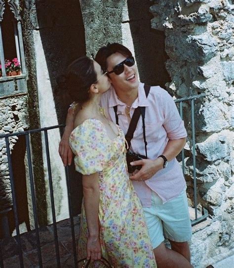 A Man And Woman Standing Next To Each Other In Front Of A Stone Wall