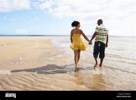 Romantic Young Couple Walking Along Shoreline Of Beach Holding Hands