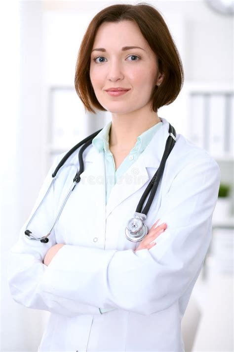 Young Brunette Female Doctor Standing With Arms Crossed And Smiling At