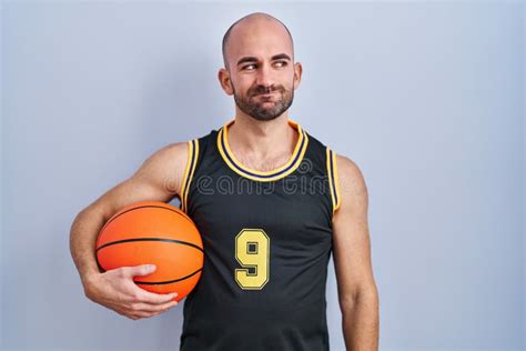 Young Bald Man With Beard Wearing Basketball Uniform Holding Ball