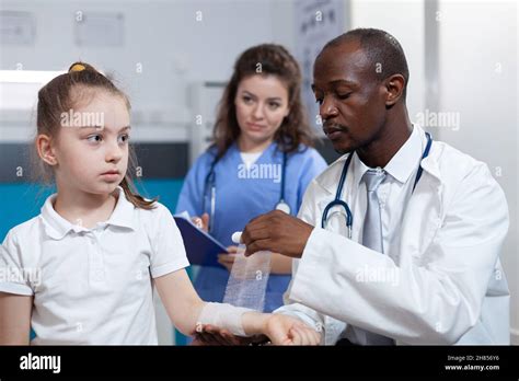 African American Pediatrician Doctor Bandage Fractured Arm Of Girl