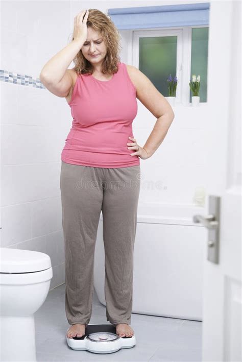 Overweight Woman Weighing Herself On Scales In Bathroom Stock Image